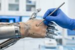 Tangan peneliti bersarung tangan medis sedang menguji respons sensor tekanan pada kulit buatan yang melapisi jari robot bionik di laboratorium.