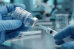 Fotografi makro realistis tangan tenaga medis bersarung tangan biru sedang menyedot cairan vaksin dari botol vial menggunakan jarum suntik, merepresentasikan inovasi vaksin kanker personal.